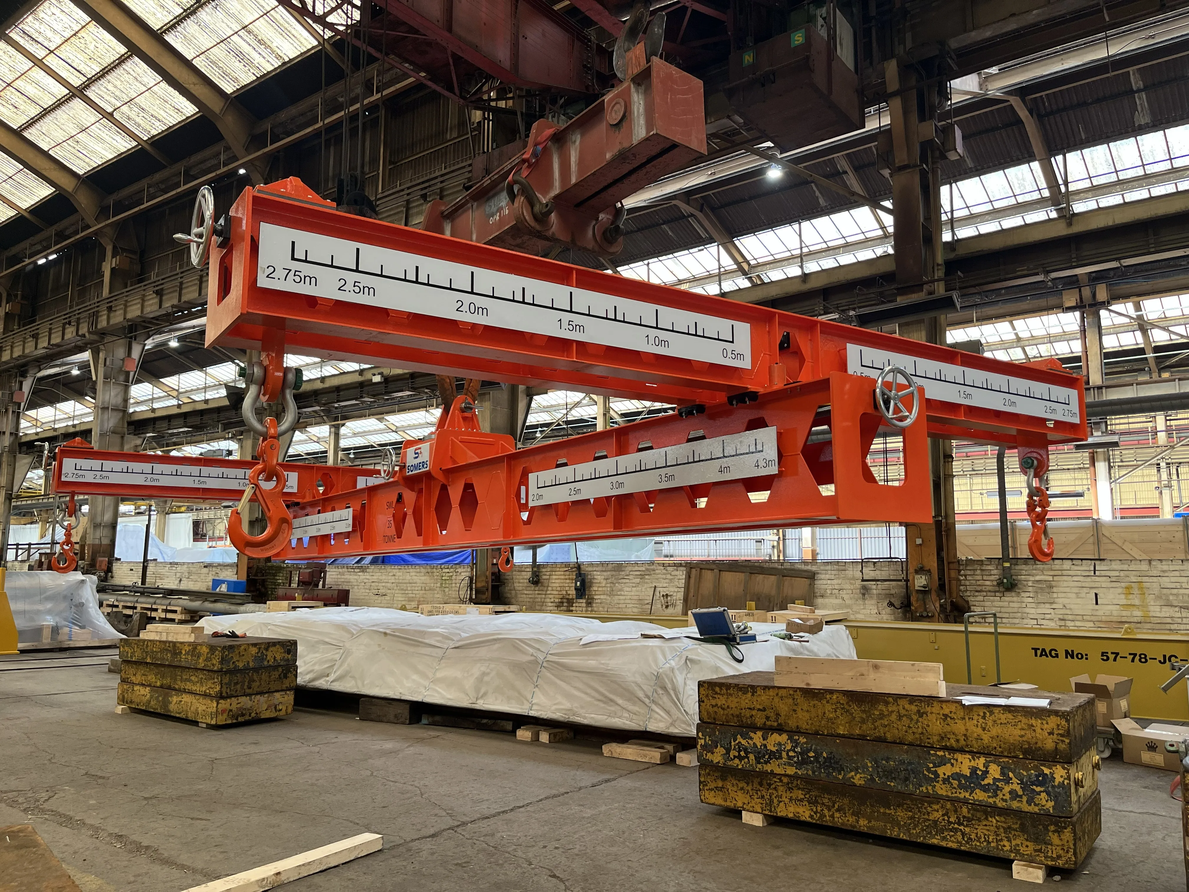 Somers Handling adjustable red lifting beam suspended in an industrial test facility, showing the adjustable spreader configuration and scale markings.